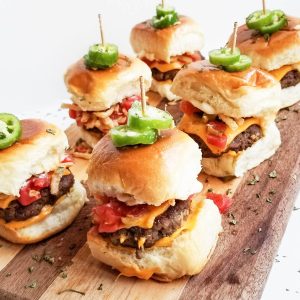hamburger slicer with american cheese, diced tomatoes, fried onions, topped with fresh jalapenos , on a wooden board