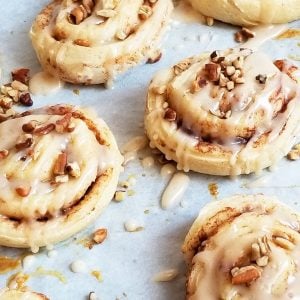 95-Calorie Ooey Gooey Cinnamon Rolls, drizzled with icing and topped with pecans on parchment paper, made with 2-Ingredient dough