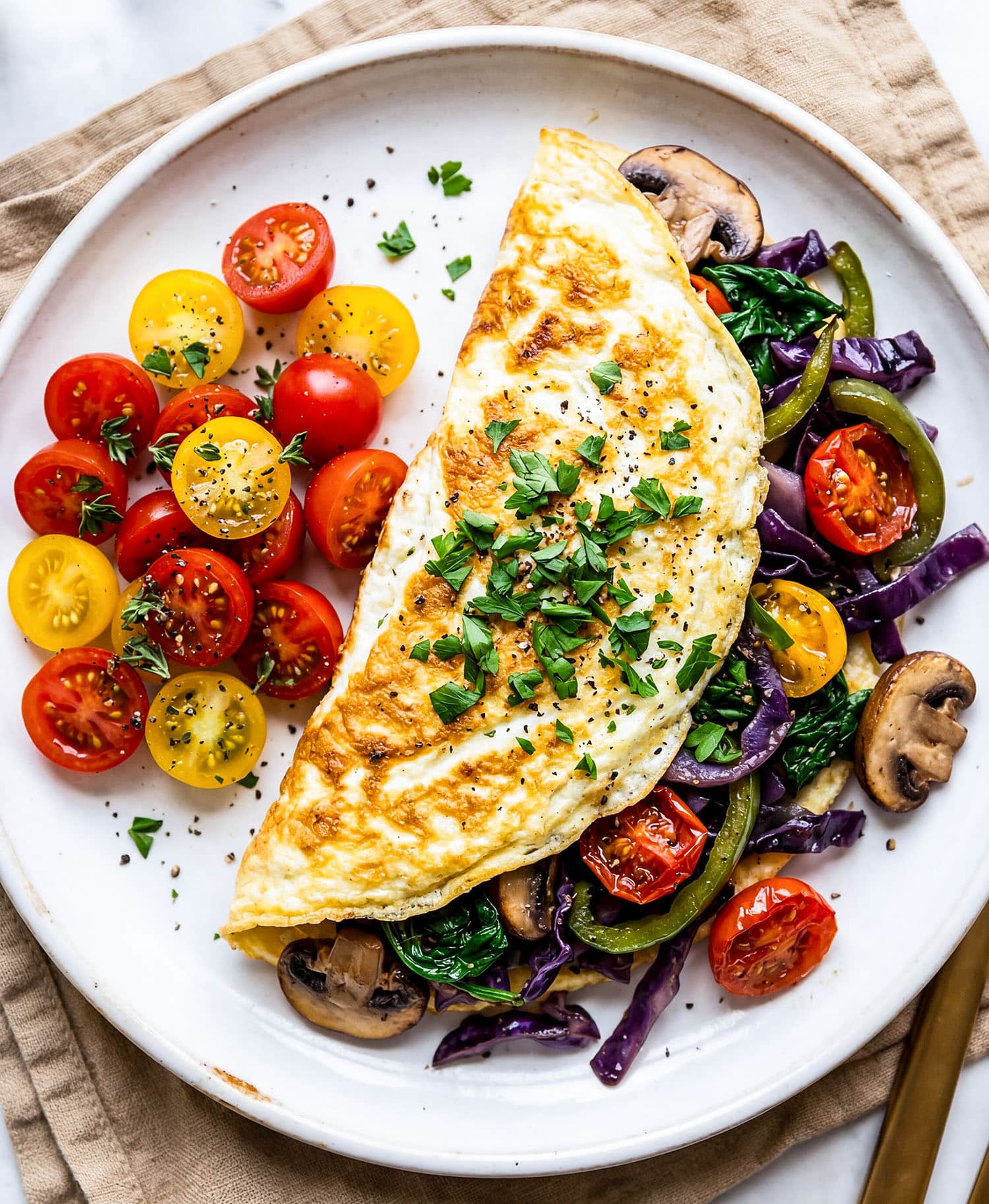 Veggie stuffed egg white omelet with spinach, peppers, mushrooms, and tomatoes on a white plate
beautifuleatsandthings.com