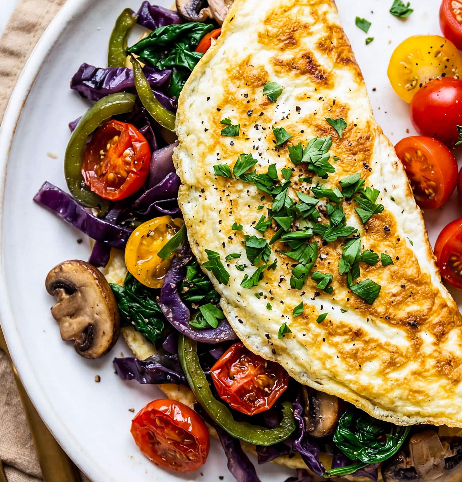 Veggie stuffed egg white omelet with spinach, peppers, mushrooms, and tomatoes on a white plate
beautifuleatsandthings.com