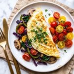 Veggie stuffed egg white omelet with spinach, peppers, mushrooms, and tomatoes on a white plate beautifuleatsandthings.com