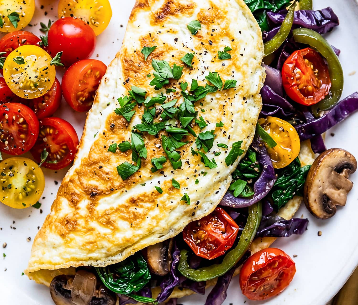 Veggie stuffed egg white omelet with spinach, peppers, mushrooms, and tomatoes on a white plate
beautifuleatsandthings.com
