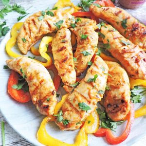 roasted pepper grilled chicken fingers made with cauliflower dreamin fresh bellies, on a white plate served with red and yellow sliced bell peppers