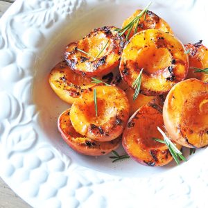 Spiced Grilled Peaches with rosemary on top served in a white bowl