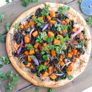 Garlicky Kale Sausage Butternut Squash Pizza-made with turkey italian sausage on a wooden board, garnished with parsley