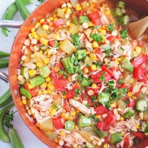 Okra, Corn, & Tomato Chicken Stew in a copper pot with a wooden spoon, topped with parsley