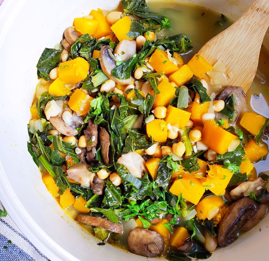 Vegan Butternut Squash, Collard Green & Chickpea Soup in a white pot with a wooden spoon