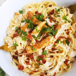 Creamy 3-Cheese Chicken & Garlic Pasta is a quick 30 minute meal served in a white bowl with chicken, bacon, and parsley on top