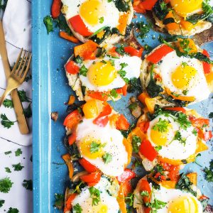 These Mini Egg & Veggie Breakfast Pizzas elevate breakfast on weekday mornings and make a quick weeknight dinner too. Mini English Muffin vegetable and sunny-side up eggs pizza on a blue sheet pan. Beautifuleatsandthings.com