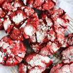 Quick Red Velvet Cake Mix Cookies, stacked on a gold wire rack with holiday scenery in the background beautifuleatsandthings.com