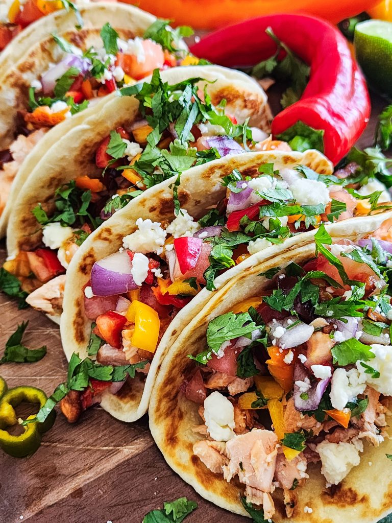 salmon tacos with a sweet pepper salsa topped with feta and cilantro on a wooden cutting board
beautifuleatsandthings.com
