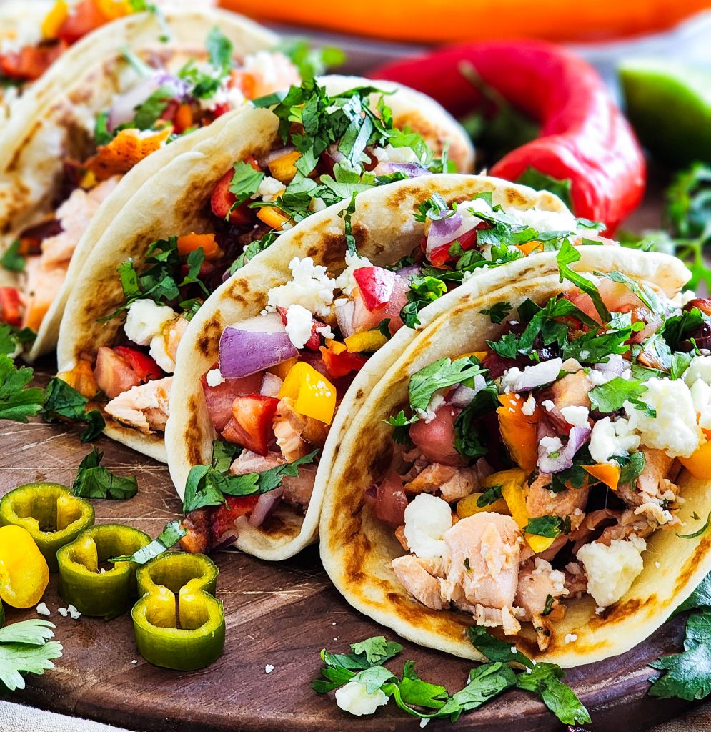 salmon tacos with a sweet pepper salsa topped with feta and cilantro on a wooden cutting board
beautifuleatsandthings.com