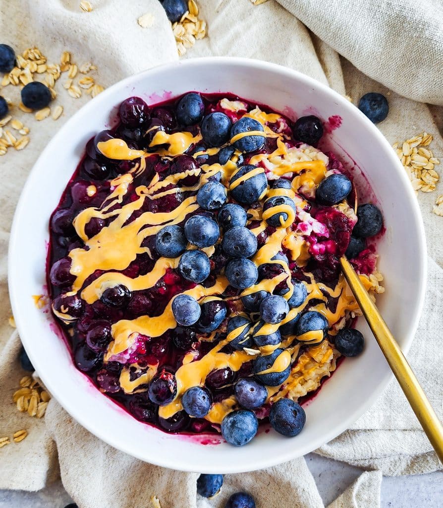 Loaded Blueberry Oatmeal topped with Peanut Butter in a white bowl, healthy breakfast