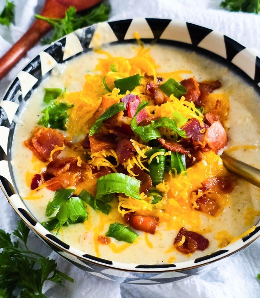Loaded Potato Crockpot Soup, made in a slow cooker, budget-friendly served in a black and white soup bowl topped with shredded cheese, bacon, and green onions
beautifuleatsandthings.com