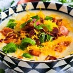 Loaded Potato Crockpot Soup, made in a slow cooker, budget-friendly served in a black and white soup bowl topped with shredded cheese, bacon, and green onions beautifuleatsandthings.com