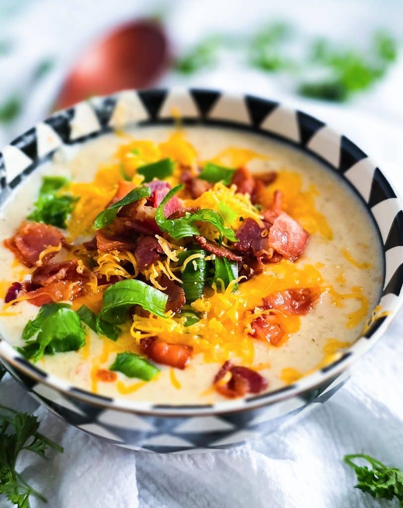 Loaded Potato Crockpot Soup, made in a slow cooker, budget-friendly served in a black and white soup bowl topped with shredded cheese, bacon, and green onions beautifuleatsandthings.com