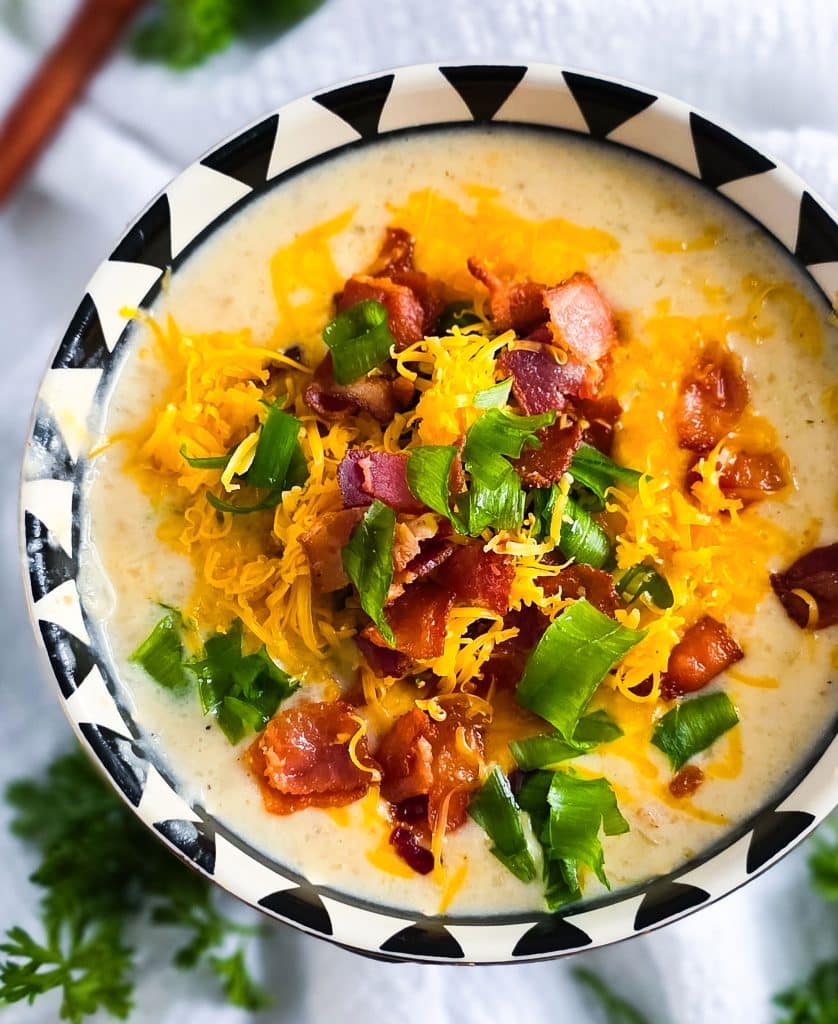 Loaded Potato Crockpot Soup, made in a slow cooker, budget-friendly served in a black and white soup bowl topped with shredded cheese, bacon, and green onions
beautifuleatsandthings.com