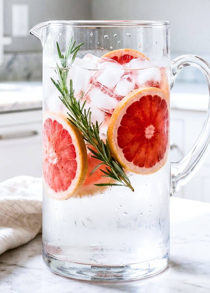 Grapefruit rosemary infused water in a glass pitcher for hydration
beautifuleatsandthings.com