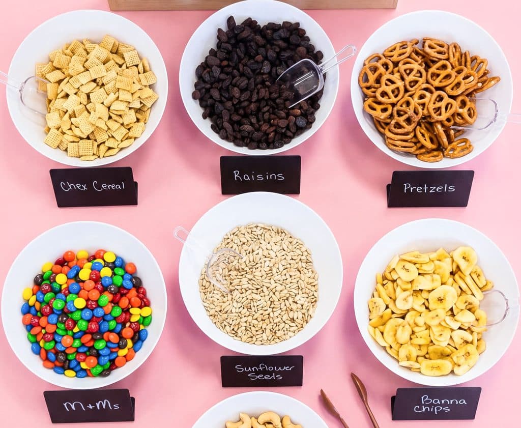 Healthy DIY trail mix station with mix-ins displayed in white bowls on a table beautifuleatsandthings.com