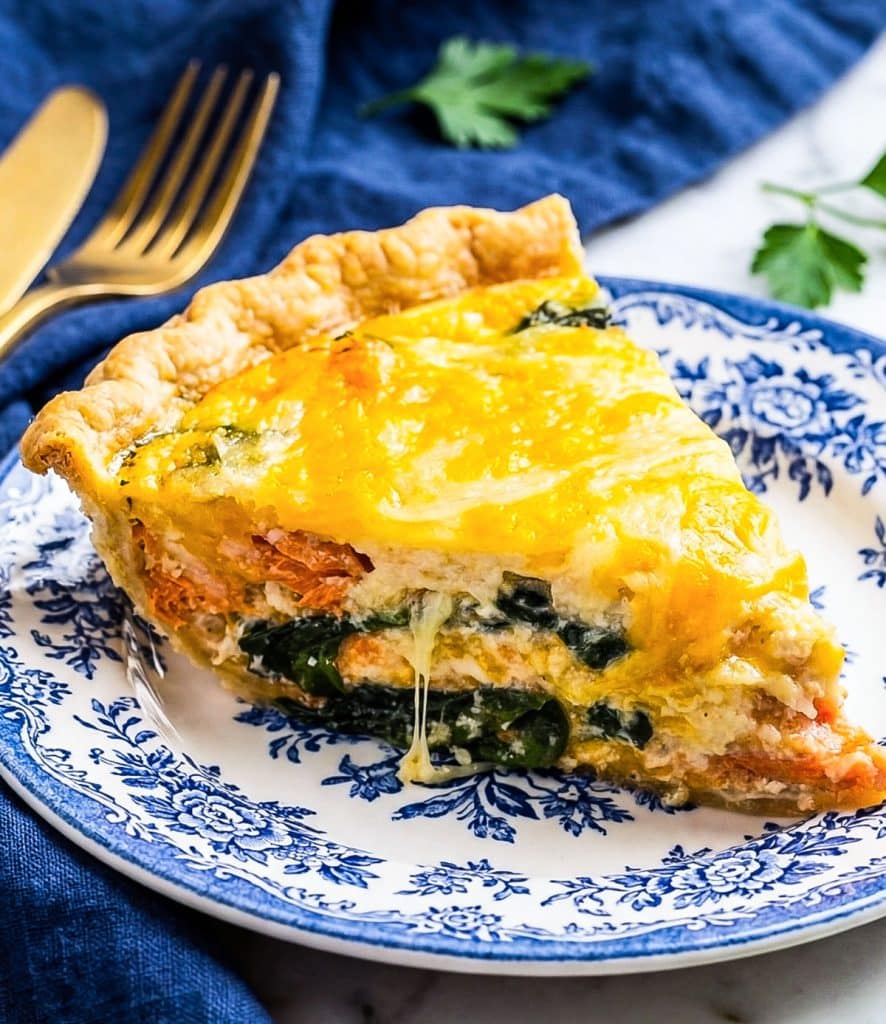 Slice of creamy salmon spinach quiche with flaky crust served on a white and blue vintage plate.
beautifuleatsandthings.com