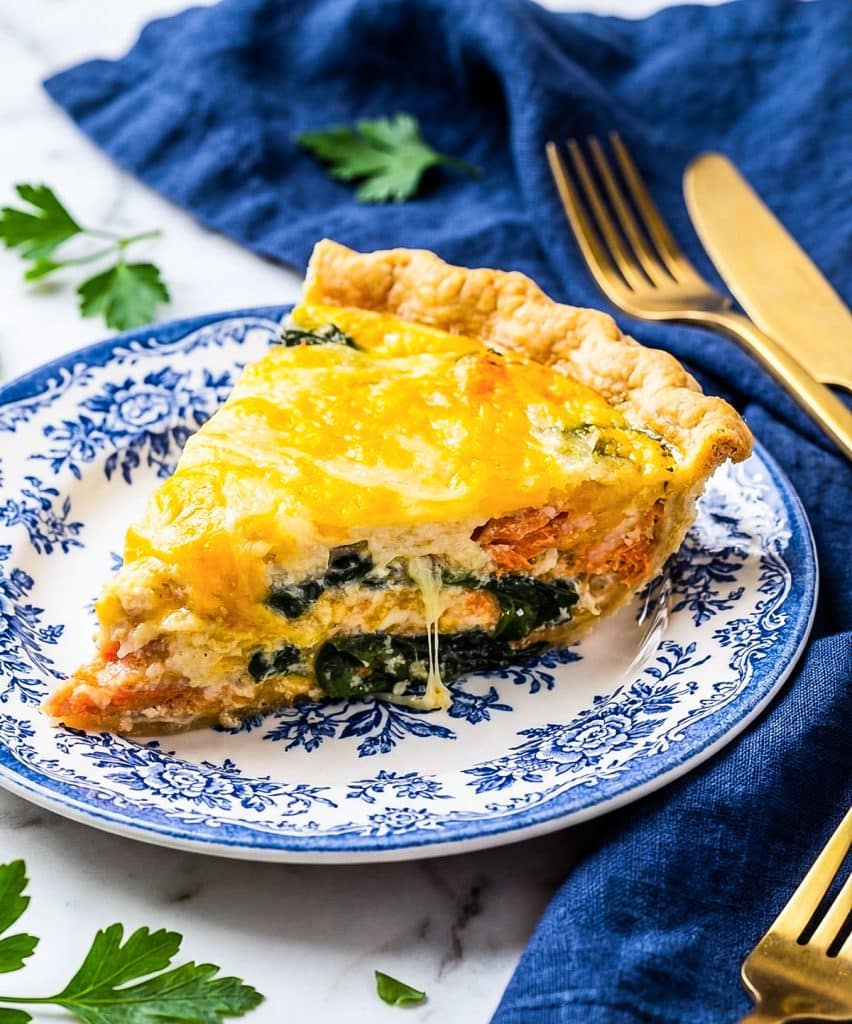 Slice of creamy salmon spinach quiche with flaky crust served on a white and blue vintage plate.
beautifuleatsandthings.com
