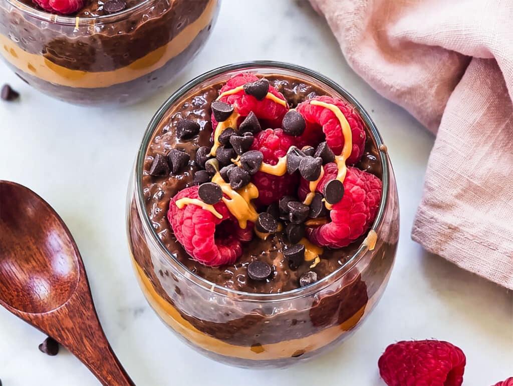 High-protein chocolate peanut butter chia pudding layered with peanut butter and topped with raspberries, chocolate chips and peanut butter drizzle.