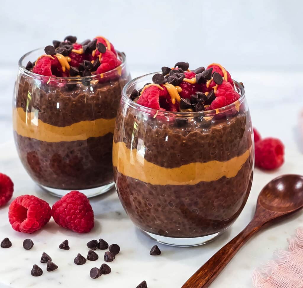 High-protein chocolate peanut butter chia pudding layered with peanut butter and topped with raspberries, chocolate chips and peanut butter drizzle.