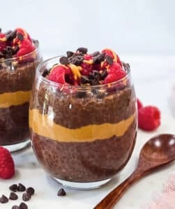 High-protein chocolate peanut butter chia pudding layered with peanut butter and topped with raspberries, chocolate chips and peanut butter drizzle.
