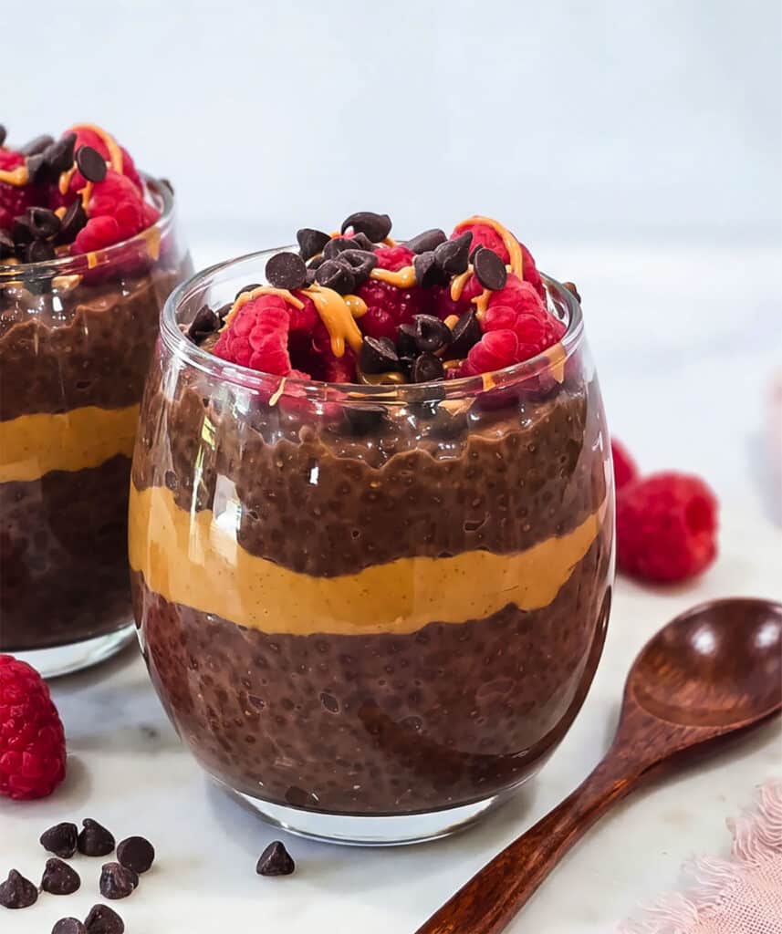 High-protein chocolate peanut butter chia pudding layered with peanut butter and topped with raspberries, chocolate chips and peanut butter drizzle.
