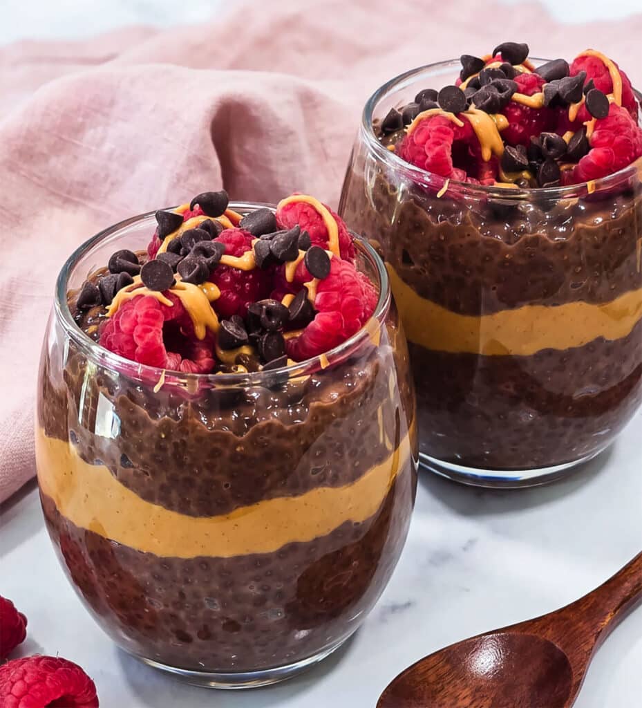 High-protein chocolate peanut butter chia pudding layered with peanut butter and topped with raspberries, chocolate chips and peanut butter drizzle.