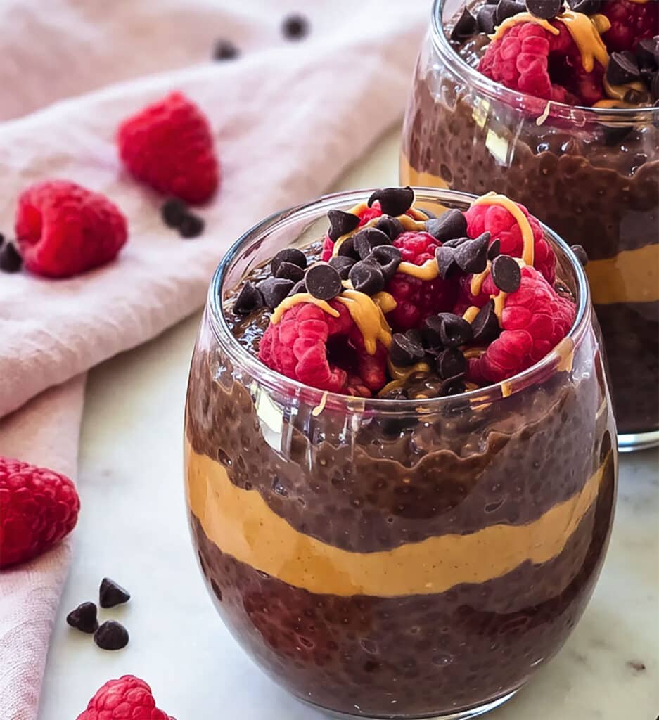 High-protein chocolate peanut butter chia pudding layered with peanut butter and topped with raspberries, chocolate chips and peanut butter drizzle.